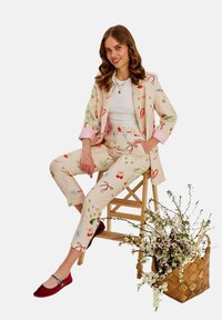 Jasnoszary garnitur z kolorowymi wzorami, w tym kwiatami i kokardkami. Składa się z dopasowanej marynarki i zwężających się spodni, do których dobrano czerwone baleriny.