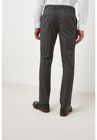 Pantalones de traje gris con un corte ajustado, que presentan una textura suave y sutiles rayas en espiga. Acentos de bolsillo trasero con cierres de botón.
