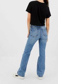 Jeans in denim blu a zampa con vita alta, texture sbiadita, cinque tasche e cuciture visibili. Abbinati a una T-shirt nera corta e sneakers.