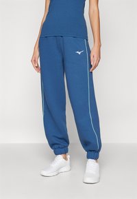 Zili adidas sporta bikses, kas izgatavotas no kokvilnas maisījuma, ar zaļām sānu svītrām un baltu logo priekšpusē, elastīgiem aprocēm un brīvu piegriezumu.
