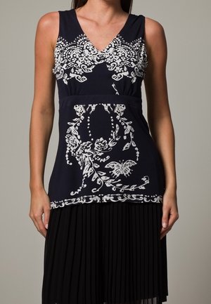 Marineblå kjole med hvide blomster- og sommerfuglemønstre. Plisseret sort nederdel. V-udskæring med en tætsiddende krop. Glat stoftekstur.