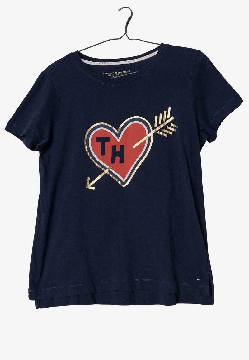 Mörkblå T-shirt med korta ärmar, med en grafik av ett röd hjärta och pilar med guldaccenter och bokstäverna "TH" i mitten.
