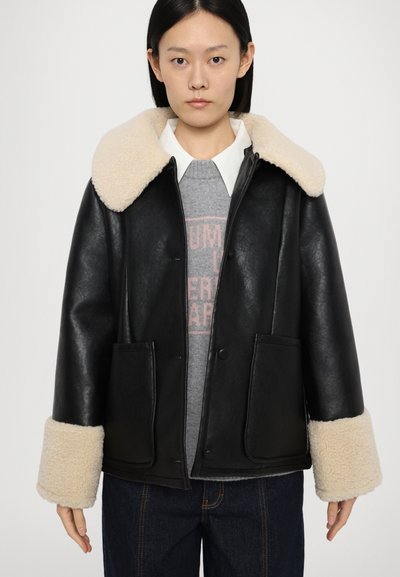 Giacca di pelle nera con un ampio colletto e polsini in pelliccia shearling color crema, dotata di due tasche frontali e chiusura con bottoni.
