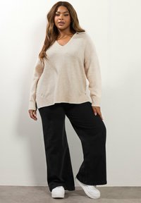 Väigne, pehmeast kudumist särk V-kaelusega ja külgserve, koos laia lõikega mustade pükstega ja valgete tossudega. Üksikasjalikult sile tekstuur.