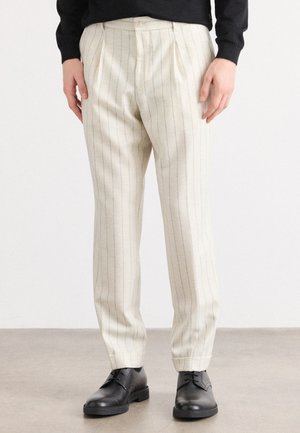 Cream-colored pleated trousers with blue pinstripes, made of a textured fabric; paired with black dress shoes.