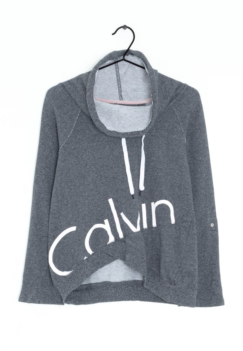 Šedá mikina s dlouhými rukávy a bílým nápisem "Calvin". Má vysoký límec, šňůrky a šikmý lem z měkké, texturované látky.