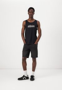 Svart tanktopp med "oblivion" trykk, kombinert med mørke denimshorts og svarte sneakers med hvite detaljer, brukt med hvite sokker.