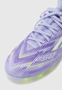 Purple and green soccer cleat with a textured surface, featuring a zigzag pattern, light laces, and visible branding "F50 Spark Fusion."