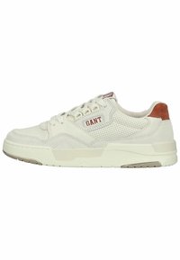 Vit sneaker tillverkad av mesh och mocka, med ett perforerat mönster, beige sula och en brun läderdetalj vid hälen. Röd logotypdetalj.