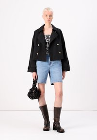 Giacca nera doppiopetto, top a quadretti senza maniche, pantaloni corti in denim blu, borsa nera текстurizzata, stivali marroni al ginocchio. Materiali lisci, look casual.