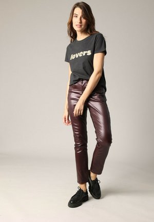 Zwarte t-shirt met de tekst "lovers" in goud, gecombineerd met bordeauxrood glanzende broeken en zwarte veterschoenen. Eenvoudig ontwerp en slim fit.