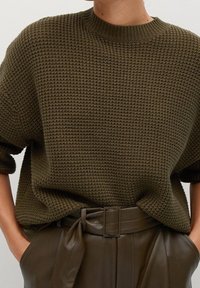 Oliwkowy sweter dzianinowy o teksturowanym, plecionym wzorze i okrągłym dekolcie, zestawiony z wysokimi skórzanymi spodniami z przewiązanym paskiem.