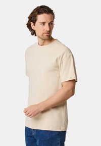 Short-sleeve beige t-shirt made of soft cotton, featuring a crew neckline and a relaxed fit, paired with blue denim jeans.