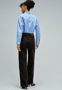 Camisa botón azul claro con yugo trasero, combinada con pantalones de pana marrón. El conjunto presenta un corte clásico y un tejido texturizado.