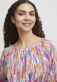 Top colorat dintr-un material ușor, cu o decolteu larg și economisire elastică, având un model vibrant cu dungi roz, galbene, albastre și albe.