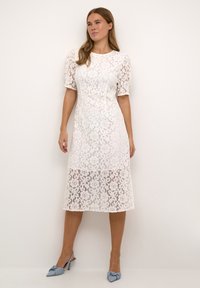 White lace midi dress with puff sleeves, floral pattern, fitted waist, and semi-sheer texture, paired with light blue pointed slingback shoes.