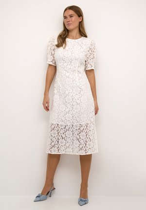 Robe midi en dentelle blanche avec des manches à volants, motif floral, taille cintrée et texture semi-transparente, assortie à des chaussures slingback pointues légèrement bleues.