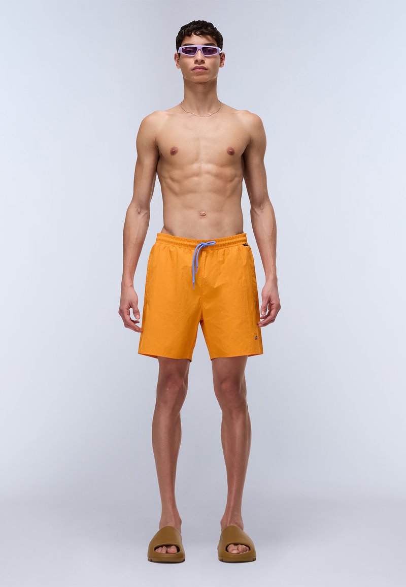 Shorts de bain orange vif avec ceinture élastique et cordon de serrage bleu, associés à des sandales marron et des lunettes de soleil teintées de violet.