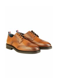 Braune Leder-Brogues mit dekorativen Perforationen, einer runden Zehenpartie, dunkler Sohle und kontrastierenden Absatzakzenten in Rot und Navy.