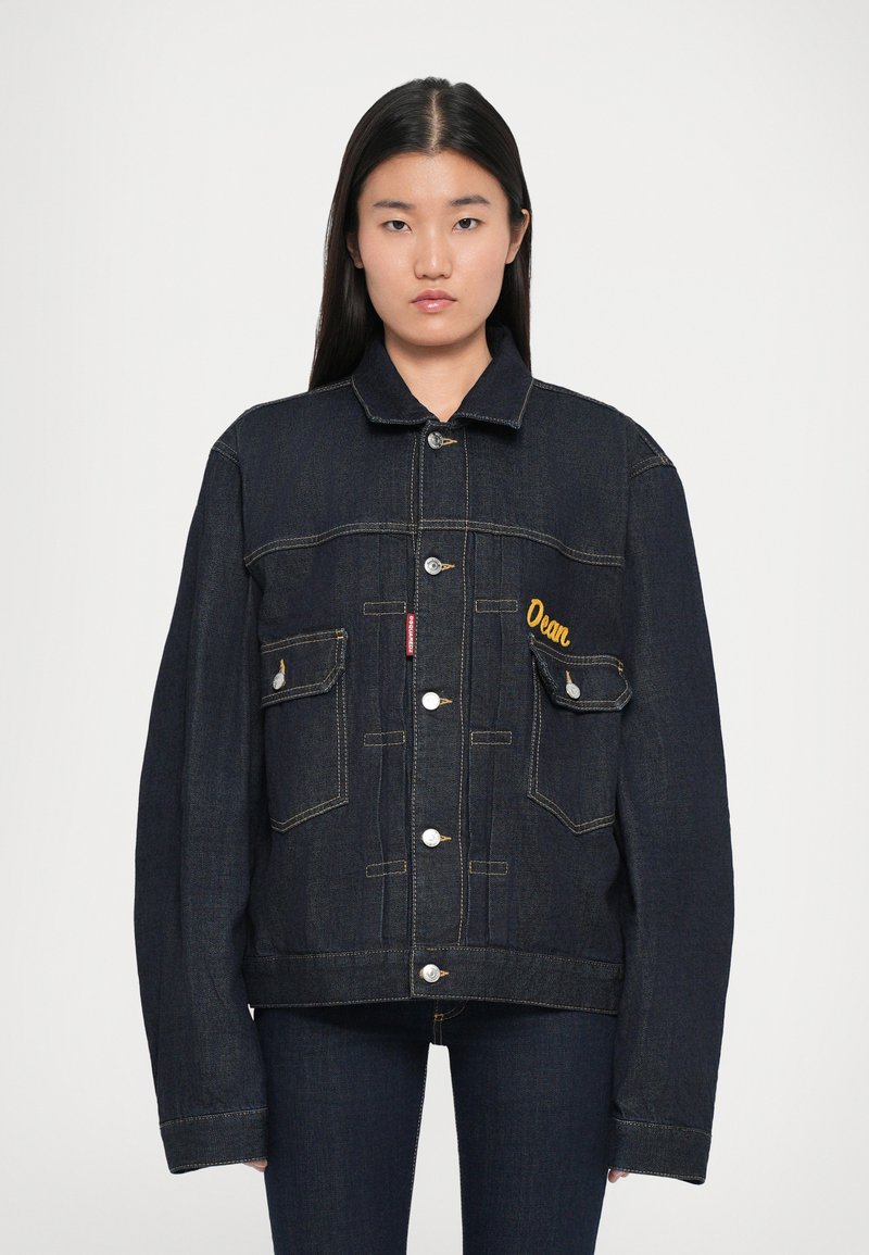 Veste en denim noir avec un devant à boutons, deux poches poitrine et broderies jaunes. Présente des manches larges et des coutures contrastées.