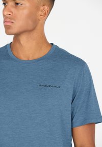 Sininen lyhythihainen t-paita, joka on valmistettu pehmeästä, teksturoidusta kankaasta. Ominaisuuksiin kuuluu pyöreä pääntie ja musta "ENDURANCE" -logo painettuna rintaan.