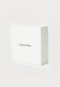 Witte rechthoekige doos met een gladde textuur, met het logo "Calvin Klein" gedrukt in een strakke, moderne lettertype op de voorkant.