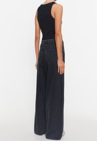 Musta ribbineulottu hihaton paita yhdistettynä leveälahkeisiin tummiin farkkuihin. Farkuissa on kaksi takataskua ja rento siluetti.