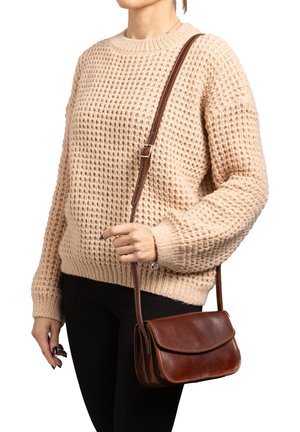 Bruine leren crossbody tas met een klep sluiting, zichtbare stiksels en een verstelbare strap, gecombineerd met een beige gebreide trui met textuur.