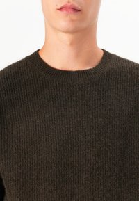 O suéter de malha verde-oliva escuro apresenta uma textura canelada, decote redondo e um brilho subtil, destacando um material grosso e macio.