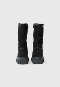 Botas de camurça pretas até ao joelho com um acabamento texturizado, apresentando um forro em pelúcia sintética, sola de borracha grossa e detalhes em costura prateada.