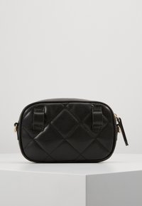 Svart läderhandväska med quiltad textur, oval form, två handtag upptill och detaljer i guldton. Minimalistisk design, kompakt storlek.