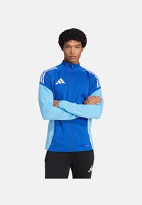 Blaues Polyester-Sportjackett mit hellblauen Ärmeln, weißen Streifen, hohem Kragen, durchgehendem Reißverschluss und Logodetail auf der Brust.