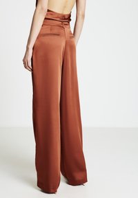 Hosen mit weitem Bein in Rostfarbe aus Satin mit glatter Textur, ausgestattet mit Gesäßtaschen und einem taillierten Design.