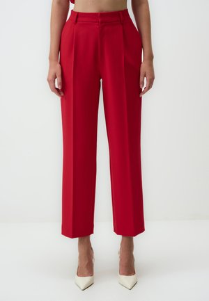 Red tailored trousers with a high waist, pleated front, straight legs, and a smooth fabric texture. Worn with white pointed heels.