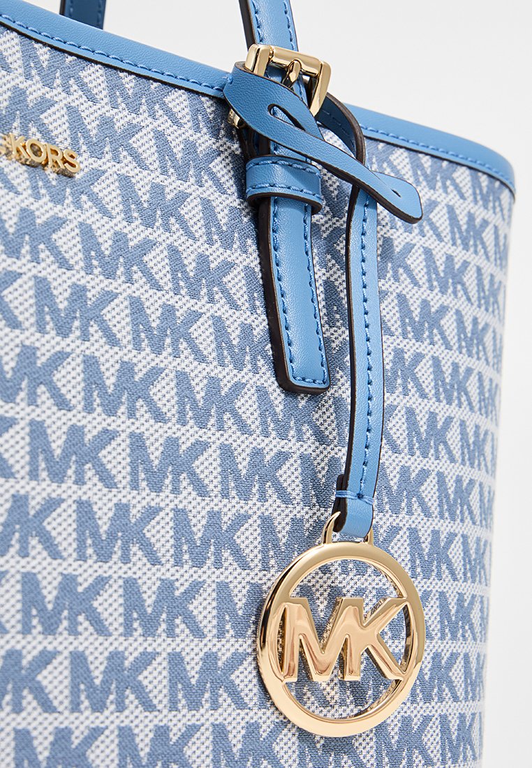 Borsa a tracolla in pelle blu con un motivo ripetuto MK, caratterizzata da dettagli in oro e una tracolla blu a contrasto. Nota pendant circolare con il logo MK.