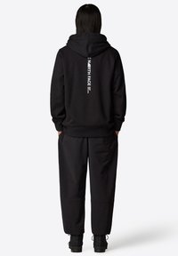 Svart hoodies med en stor, vertikal vit logotyp på baksidan. Gjord av ett mjukt material, med en avslappnad passform och ribbade ärmslut.