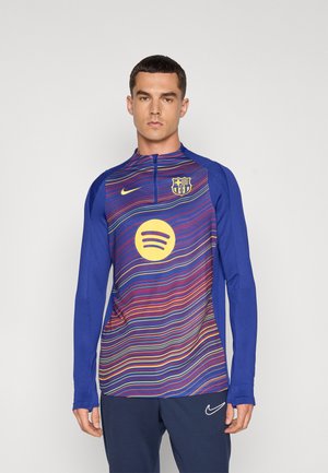 T-shirt de sport à manches longues bleu avec des lignes ondulées multicolores, un logo circulaire jaune et un petit blason d'équipe sur la poitrine.