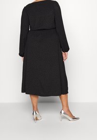 Svart midiklänning med långa ärmar, texturerad tyg och prickmönster. Matchad med silverfärgade högklackade skor.