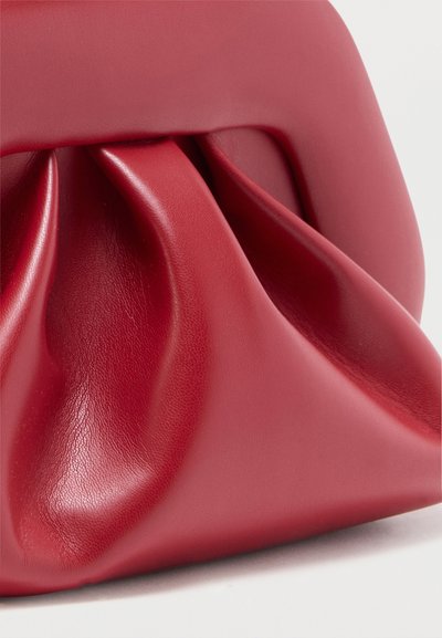 Κόκκινη δερμάτινη τσάντα χειρός με σχεδιασμό συγκεντρωμένων και πιεταριστών πτυχών και ομαλή υφή, σε απλό ανοιχτό φόντο.