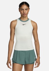 Nike mouwloos shirt in crème met een teal kraag; voorzien van een klein zwart logo. Gecombineerd met teal shorts, die een strakke, atletische pasvorm tonen.