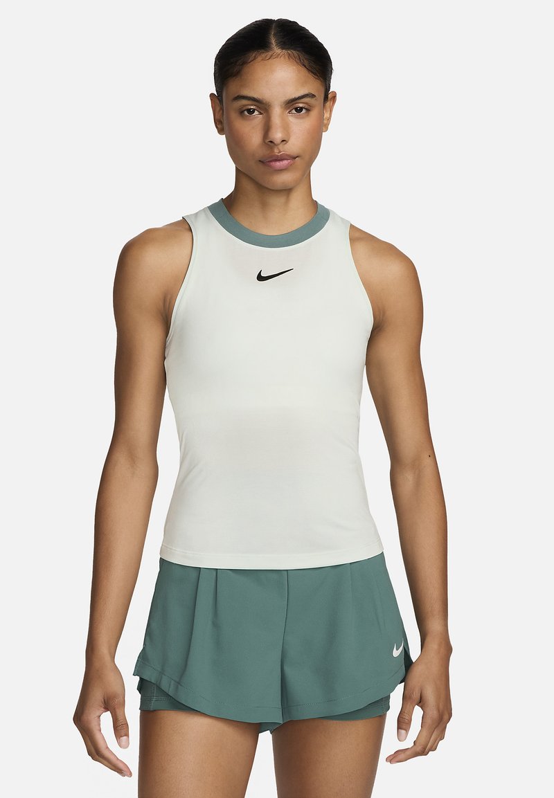 Nike mouwloos shirt in crème met een teal kraag; voorzien van een klein zwart logo. Gecombineerd met teal shorts, die een strakke, atletische pasvorm tonen.