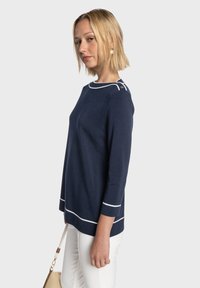 Pull en maille bleu marine avec manches trois-quarts, détails contrastants blancs au niveau de l'encolure et de l'ourlet, présentant un tissu texturé.