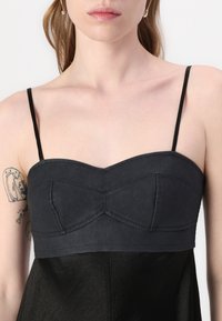 Svart tilpasset crop top med tynne stropper, med en teksturert overflate og strukturert design med dart-sømmer på et glatt stofflag.