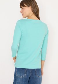 Top de manga larga en verde menta con escote redondo y aberturas laterales, combinado con pantalones de mezclilla azul que tienen bolsillos traseros. Textura suave.