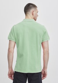Mentazöld polo ing, rövid ujjakkal és gallérral, egyenes szegéllyel és bordázott díszítéssel az ujjakon. Nincsenek látható minták vagy kiemelések.