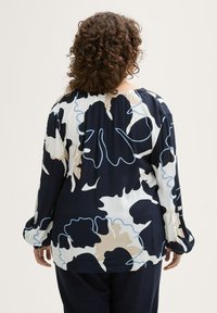 Bedruckte Bluse mit navy Hintergrund, die große florale Muster in Creme und Hellblau zeigt. Lange Ärmel und gerafftes Halsdetail.