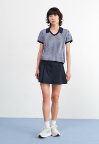 Short-sleeve navy and white patterned polo shirt paired with a black flared skirt, worn with white socks and light-colored athletic shoes.