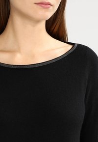 Maglione nero con un ampio scollo, texture a coste e un accento argentato lungo il colletto. Il tessuto appare morbido e aderente.