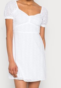 Vit bomullsklänning med korta puffärmar, fyrkantig halsringning och broderi med ögonlock, med en åtsittande bodice och flytande kjol.