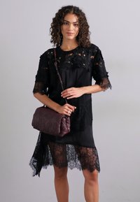 Black dress with lace sleeves and hem, featuring intricate floral patterns. Paired with a burgundy handbag with textured accents.